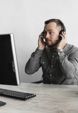Genç işadamı ya da öğrenci bir gömlek kulaklık bilgisayar monitörü karşı oturan ve internet üzerinden biriyle konuşuyor. Ofisteki bir masada bir bilgisayar üzerinde çalışmak.