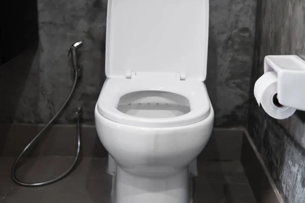 White hanging toilet seat on white toilet in the home bathroom with grey tiles in concrete style and toilet paper on the wall. Bathroom luxury interior. — Stock Photo, Image