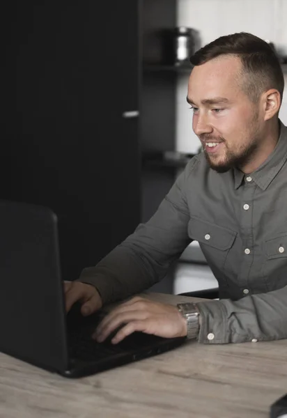 Ευτυχισμένο χαμόγελο νέος επιχειρηματίας ή φοιτητής σε ένα πουκάμισο που κάθεται ενάντια στην οθόνη του υπολογιστή. Εργασία σε έναν υπολογιστή σε έναν πίνακα στο γραφείο με μια προσεκτική έκφραση. — Φωτογραφία Αρχείου