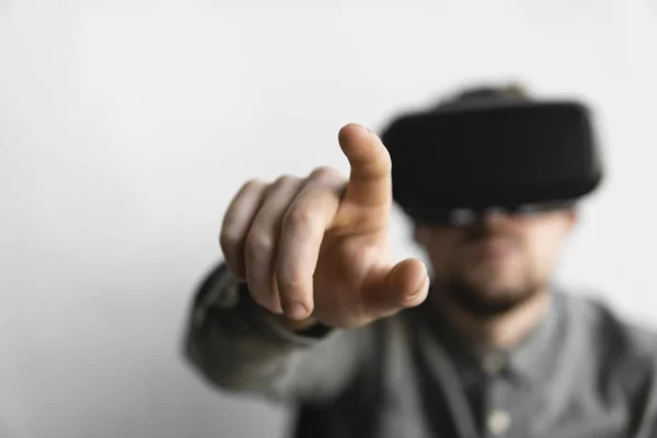 Young bearded man with virtual reality glasses trying to touch something or tap some thing in front of what he seeing. Modern technologies. The concept of future technology.