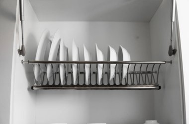 Bulaşık kurutucu metal raf ve büyük beyaz tabaklar. Geleneksel rahat mutfak. İçinde ıslak cam ve seramik tabaklar, tabaklar ve kaseler olan beyaz tabak kurutma dolabını aç..