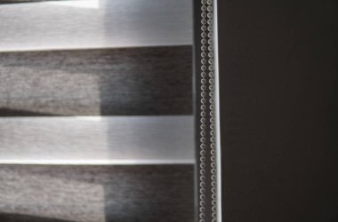 Oturma odasındaki ahşap desenli plastik camdaki kahverengi kumaş jaluzilerinin detayları..