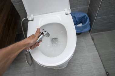 Beyaz tuvaletli bide duşu kullanmak. Beyaz klozet kullandıkları için erkek ellerinde bidet banyosu..