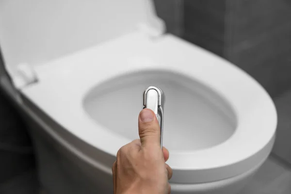 Using of bidet shower with a white toilet. Bidet shower in male hand for using with a white toilet bowl. — Stock Photo, Image