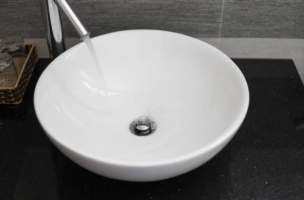 在现代化的浴室里有白色圆形水槽和铬水龙头的浴室内部。 从铬水龙头流出的水. — 图库照片