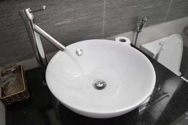 Bathroom interior with white round sink and chrome faucet in a modern bathroom. Water flowing from the chrome faucet. — ストック写真