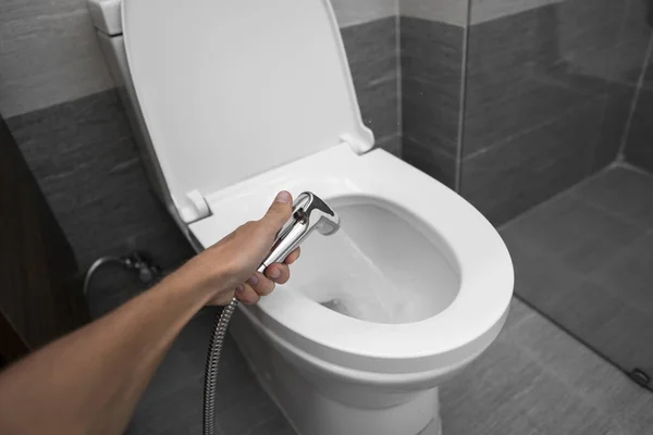 Menggunakan shower bidet dengan toilet putih. Hujan lelang di tangan laki-laki untuk digunakan dengan toilet putih mangkuk . — Stok Foto