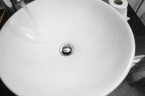 Intérieur de la salle de bain avec lavabo rond blanc et robinet chromé dans une salle de bain moderne. Eau qui coule du robinet chromé . — Photo