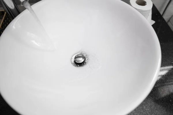 Interior del cuarto de baño con lavabo redondo blanco y grifo de cromo en un baño moderno. Agua que fluye del grifo de cromo . —  Fotos de Stock