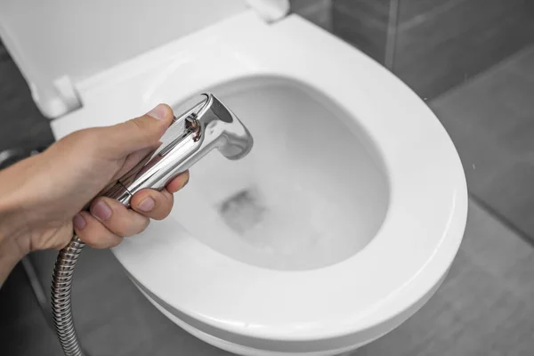 Utilisation d'une douche bidet avec toilettes blanches. Douche Bidet à la main masculine pour utilisation avec un bol de toilette blanc . — Photo