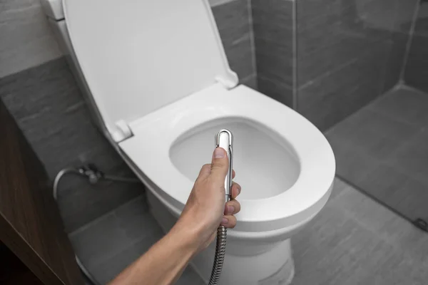 Utilisation d'une douche bidet avec toilettes blanches. Douche Bidet à la main masculine pour utilisation avec un bol de toilette blanc . — Photo