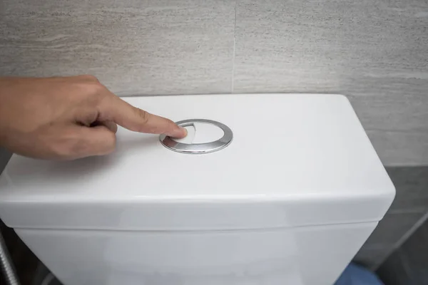 Zamknij palec wciskając spłukany przycisk toalety do czyszczenia toalety. — Zdjęcie stockowe