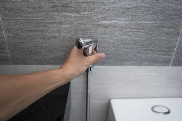 Использование биде-душа в ванной комнате с биде или туалетом. Биде душ в мужской руке для использования его в ванной комнате . — стоковое фото