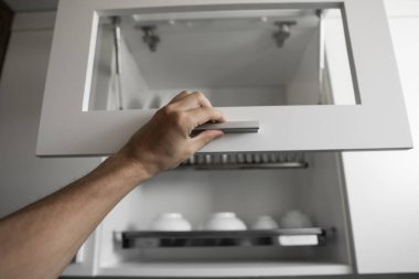 El, kurutma makinesinin kapısını çatal bıçakla tutuyor. Tabak kurutucu metal raf ve beyaz temiz tabaklar. Geleneksel rahat mutfak. Islak tabak ve kâselerle dolu beyaz tabak boşaltma dolabını aç..