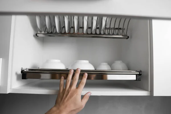 Dish drying metal rack with big nice white clean plates. Traditional comfortable kitchen. Open white dish draining closet with wet dishes of glass and ceramic, plates, bowls drying inside on rack. — Stock Photo, Image