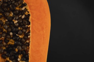 Olgun papayanın yarısı siyah tabakta tohum ve arka planda yeşil bitkiler. Tatlı papaya dilimleri. Yarım papayalar. Sağlıklı egzotik meyveler. Vejetaryen yemeği..