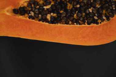 Olgun papayanın yarısı siyah tabakta tohum ve arka planda yeşil bitkiler. Tatlı papaya dilimleri. Yarım papayalar. Sağlıklı egzotik meyveler. Vejetaryen yemeği..