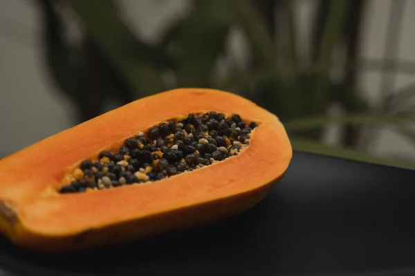 Half of ripe papaya with seed on a black plates and with a green plants on background. Slices of sweet papaya. Halved papayas. Healthy exotic fruits. Vegetarian food. — ストック写真