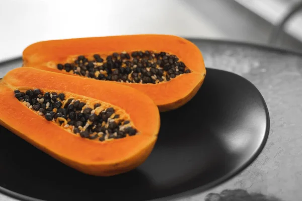 Two half of ripe papaya with seeds in a black plate on a glass table with a white background. Slices of sweet papaya. Halved papayas. Healthy exotic fruits. Vegetarian food. — ストック写真