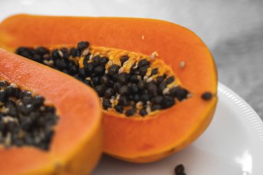 Beyaz bir tabakta tohum ile yarısı kesilmiş papaya. Beyaz arkaplanı olan tatlı papaya dilimleri. Yarım papayalar. Sağlıklı egzotik meyveler. Vejetaryen yemeği..