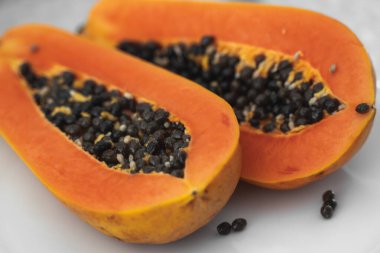 Beyaz bir tabakta tohum ile yarısı kesilmiş papaya. Beyaz arkaplanı olan tatlı papaya dilimleri. Yarım papayalar. Sağlıklı egzotik meyveler. Vejetaryen yemeği..