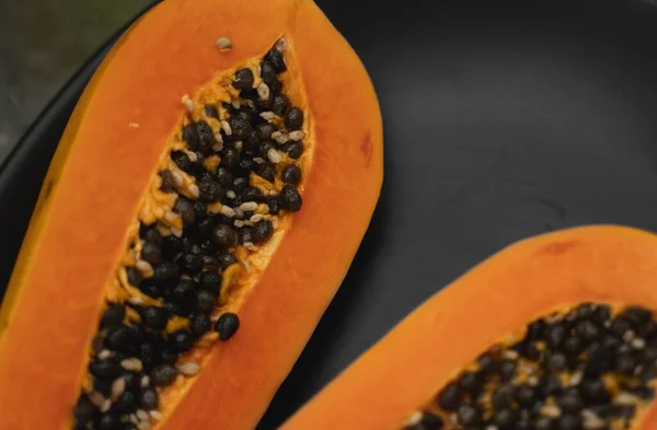 Half of ripe papaya with seed on a black plates and with a green plants on background. Slices of sweet papaya. Halved papayas. Healthy exotic fruits. Vegetarian food. — ストック写真