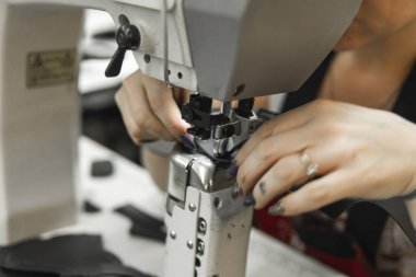 Deri atölyesinde dikiş makinesi çalışıyor. Elleri ayakkabı için deri detaylar üzerinde çalışıyor. Ayakkabı fabrikasında dikiş makinesi olan kadınların elleri..