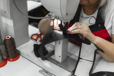 Deri atölyesinde dikiş makinesi çalışıyor. Elleri ayakkabı için deri detaylar üzerinde çalışıyor. Ayakkabı fabrikasında dikiş makinesi olan kadınların elleri..