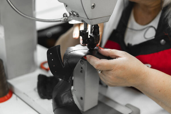 Sewing machine in a leather workshop in action with hands working on a leather details for shoes. Womens hands with sewing machine at shoes factory.