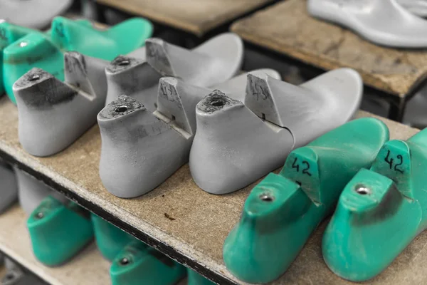 Пластик используется при производстве обуви. Ряд пластиковых ботинок используется для производства современной обуви. Много пластиковой последней туфли на деревянной полке. Оборудование, используемое для дизайна обуви . — стоковое фото