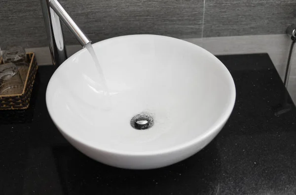 Bathroom interior with white round sink and chrome faucet in a modern bathroom. Water flowing from the chrome faucet. — ストック写真