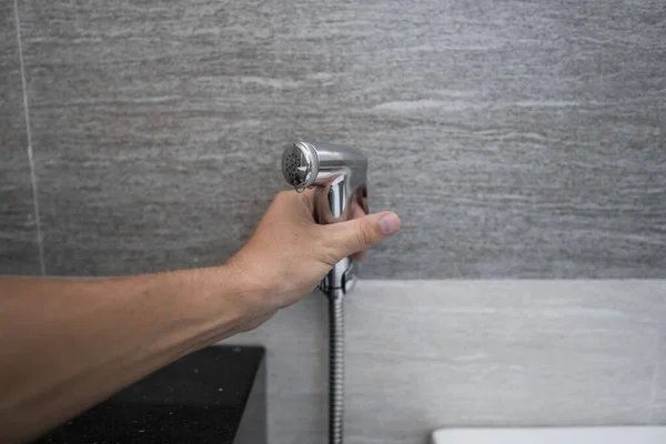 Korzystanie z bidetu prysznic w łazience z bidetem lub toilerem. Bidet prysznic w męskiej ręce do korzystania z niego w łazience. — Zdjęcie stockowe