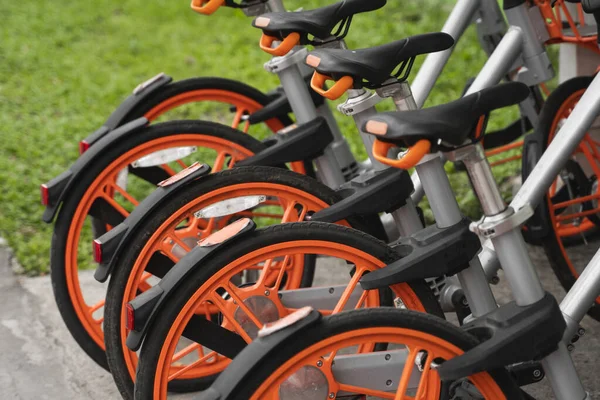 Straßenverkehr orangefarbene Hybrid-Leihräder mit elektronischer Zahlungsmethode für die Fahrt durch die Stadt stehen in Reihe auf dem Mietnetzparkplatz und warten auf Radfahrer, die mit dem Fahrrad unterwegs sind. — Stockfoto