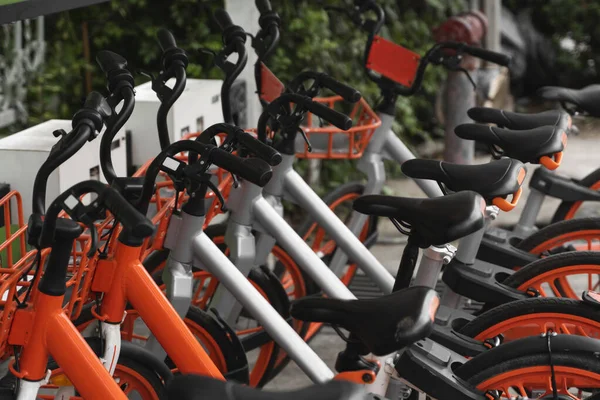 Straßenverkehr orangefarbene Hybrid-Leihräder mit elektronischer Zahlungsmethode für die Fahrt durch die Stadt stehen in Reihe auf dem Mietnetzparkplatz und warten auf Radfahrer, die mit dem Fahrrad unterwegs sind. — Stockfoto