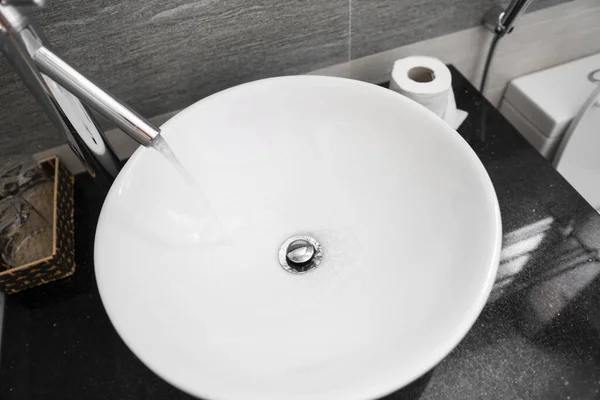 Interior del cuarto de baño con lavabo redondo blanco y grifo de cromo en un baño moderno. Agua que fluye del grifo de cromo . —  Fotos de Stock