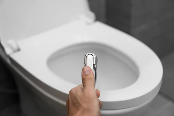 Χρήση μπιντέ ντους με λευκή τουαλέτα. Μπιντέ ντους στο αρσενικό χέρι για χρήση με ένα λευκό λεκάνη τουαλέτας. — Φωτογραφία Αρχείου