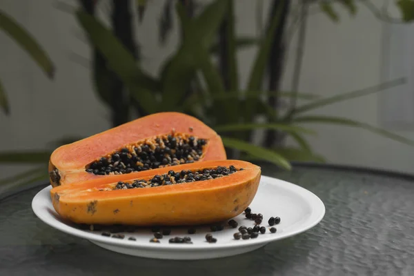 Half of ripe papaya with seed on a white plates and with a green plants on background. Slices of sweet papaya. Halved papayas. Healthy exotic fruits. Vegetarian food. — ストック写真