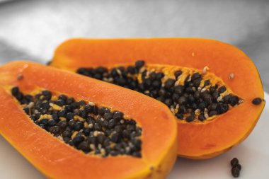 Beyaz bir tabakta tohum ile yarısı kesilmiş papaya. Beyaz arkaplanı olan tatlı papaya dilimleri. Yarım papayalar. Sağlıklı egzotik meyveler. Vejetaryen yemeği..