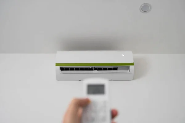 Mans hand using remote controler. Hand holding rc and adjusting temperature of air conditioner mounted on a white wall. Indooor comfort temperature. Health concepts and energy savings. — Stock Photo, Image