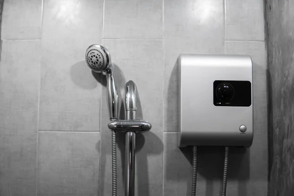 Instant tankless electric water heater installed on grey tile wall with input and output pipe outlet and elcb safety breaker system and silver shower.