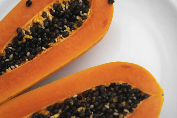 Reife Papaya mit Kernen auf einem weißen Teller halbieren. süße Papayascheiben mit weißem Hintergrund. halbierte Papayas. gesunde exotische Früchte. Vegetarisches Essen. — Stockfoto