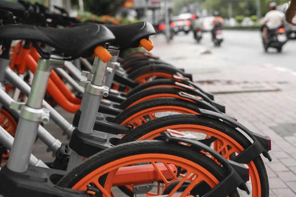 Straßenverkehr orangefarbene Hybrid-Leihräder mit elektronischer Zahlungsmethode für die Fahrt durch die Stadt stehen in Reihe auf dem Mietnetzparkplatz und warten auf Radfahrer, die mit dem Fahrrad unterwegs sind. — Stockfoto