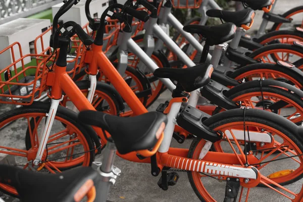 Straßenverkehr orangefarbene Hybrid-Leihräder mit elektronischer Zahlungsmethode für die Fahrt durch die Stadt stehen in Reihe auf dem Mietnetzparkplatz und warten auf Radfahrer, die mit dem Fahrrad unterwegs sind. — Stockfoto