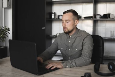 Genç işadamı ya da öğrenci bilgisayar monitörü karşı oturan bir gömlek. Düşünceli bir ifade ile ofiste bir masada bir pc üzerinde çalışıyor. Ofiste dizüstü bilgisayar üzerinde çalışan genç işadamı.
