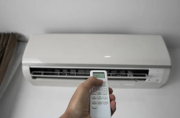 Mans hand using remote controler. Hand holding rc and adjusting temperature of air conditioner mounted on a white wall. Indooor comfort temperature. Health concepts and energy savings.