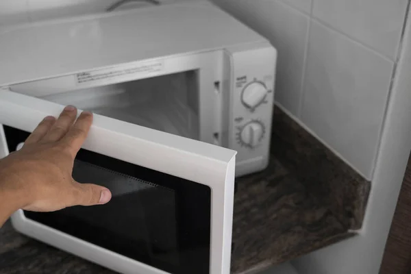 Man hand holdind a door of microwave in a kitchen for cooking or heating a dish. — Stock Photo, Image