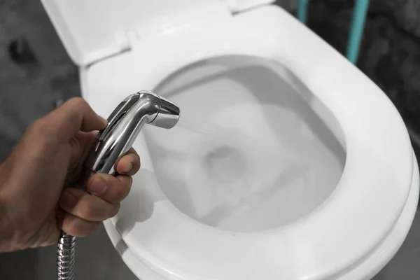 Использование биде душ с белым туалетом. Биде душ в мужской руке для использования с белой унитазом . — стоковое фото