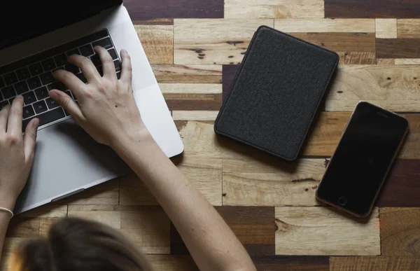 Womans hands typing on laptop keyboard top view. Study and work online, freelance. Self employed or freelance woman, girl working with her laptop sitting at wooden table with a phone and ereader.