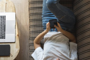 Bir kadın kanepede dizüstü bilgisayar ve masada kitap okurken akıllı telefon kullanır. Çevrimiçi çalışma, serbest çalışma. Serbest çalışan ya da serbest çalışan bir kız telefonunu kullan ve işten izin al..