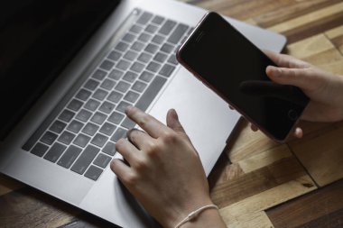 Kadın eli bilgisayarlı akıllı telefon kullanır. İnternette çalış ve çalış, serbest çalış. Serbest çalışan ya da serbest çalışan bir kadın, dizüstü bilgisayarıyla çalışan bir kız ahşap masada oturan bir telefon ve okuyucu..